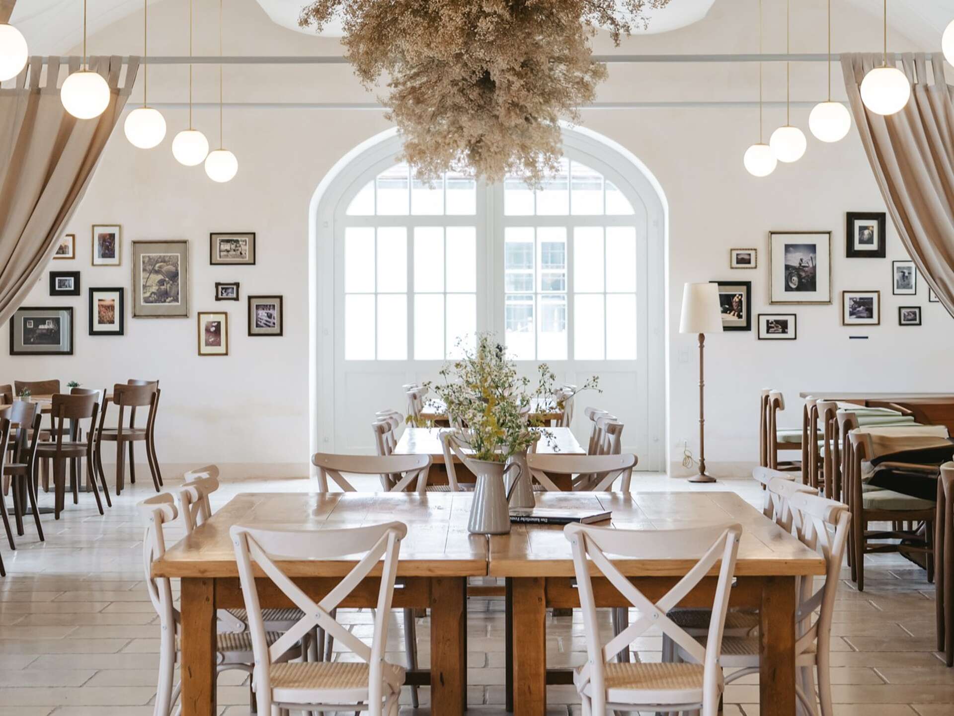 Restaurant with laid tables, pictures on the wall and flowers hanging from the ceiling