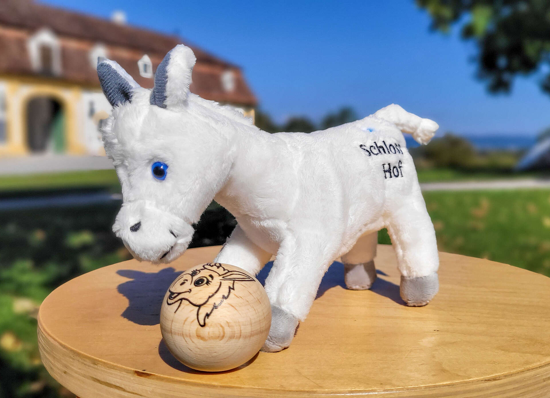Stofftier Esel steht auf einem kleinen, runden Holztisch, vor ihm ein kleiner Holzball